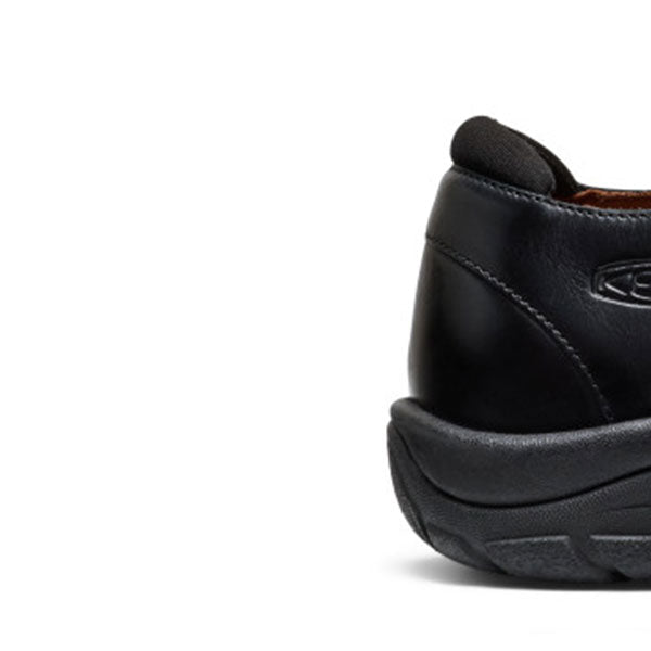 Close-up of the rear side of a black slip-on shoe, showing the heel, stitched leather upper, textured sole, and a small embossed logo on a white background.
