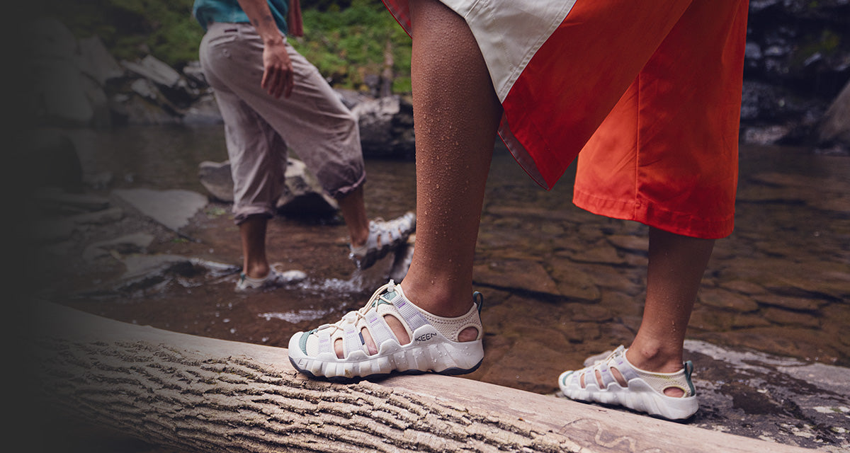 Two people wearing white sandals on a rocky path with one person in red shorts and another in beige pants.