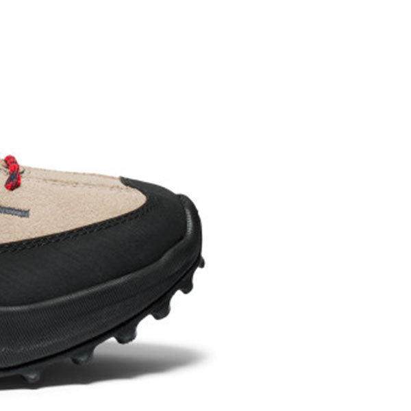 Close-up of a black and beige shoe with a red accent on a white background.