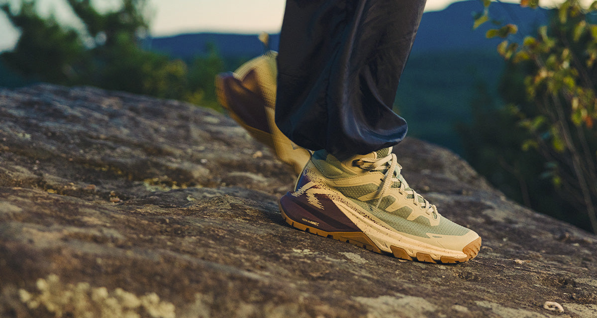 Person wearing hiking shoes on a rocky surface with a mountainous background