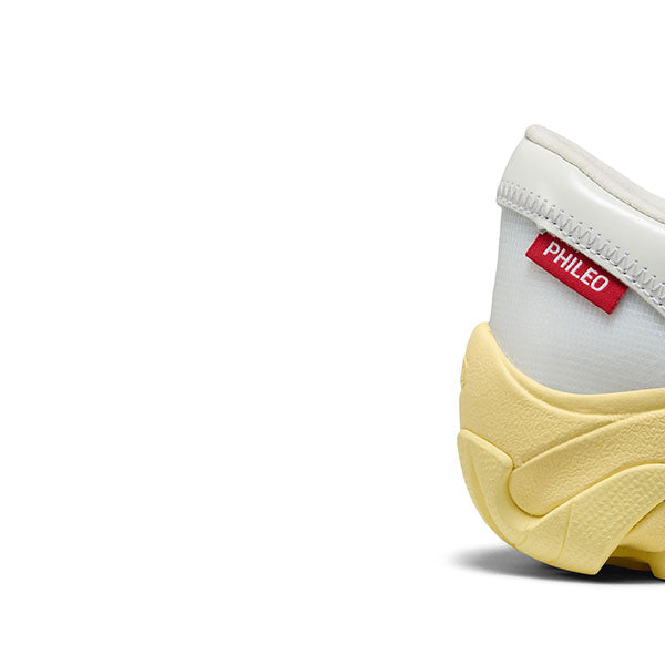 Close-up of the of the heel on the white Phileo x Keen collab shoe with a red Phileo product tag and a yellow sole on a white background